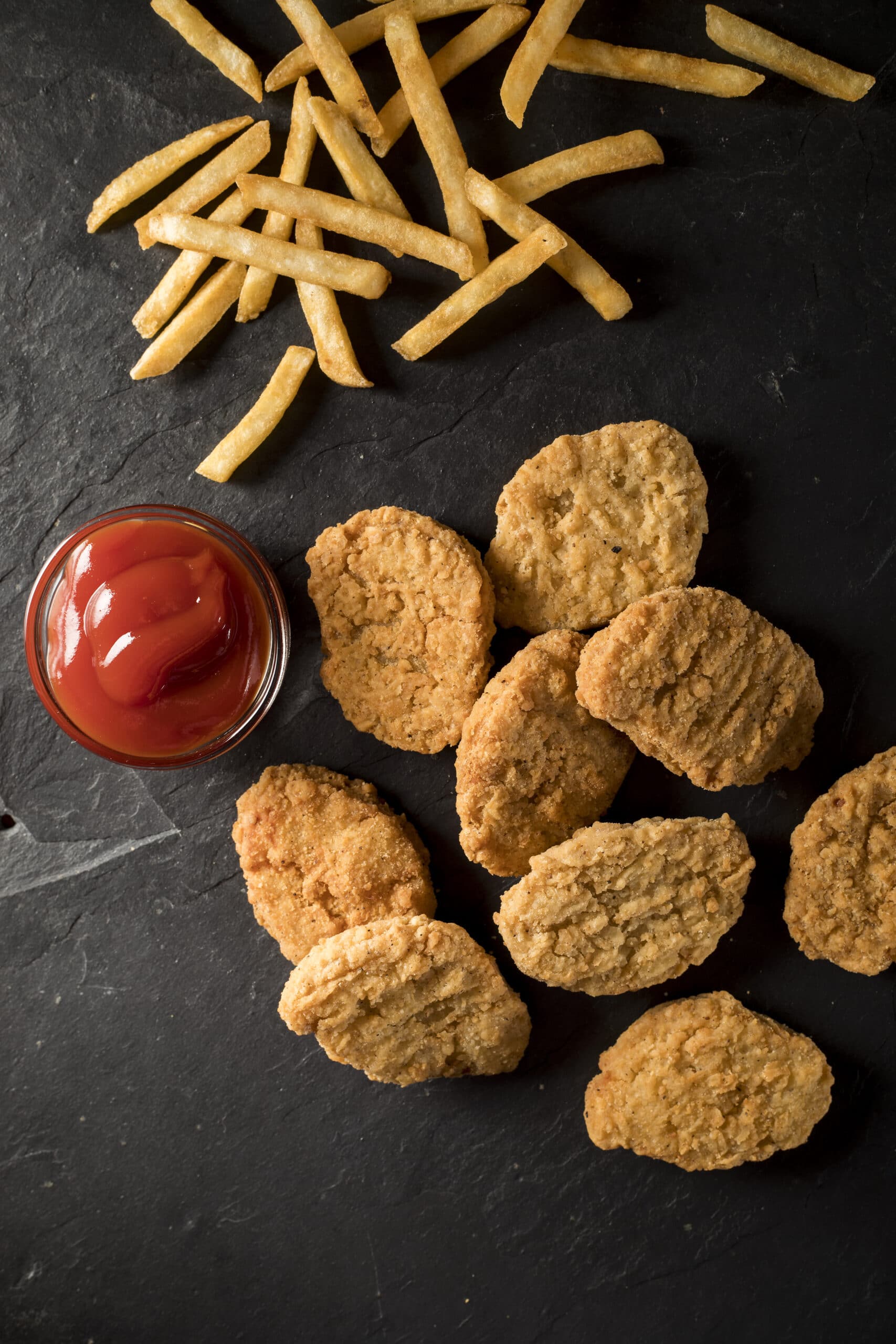 9 chicken nuggets on a slate tray with french fries and ketchup