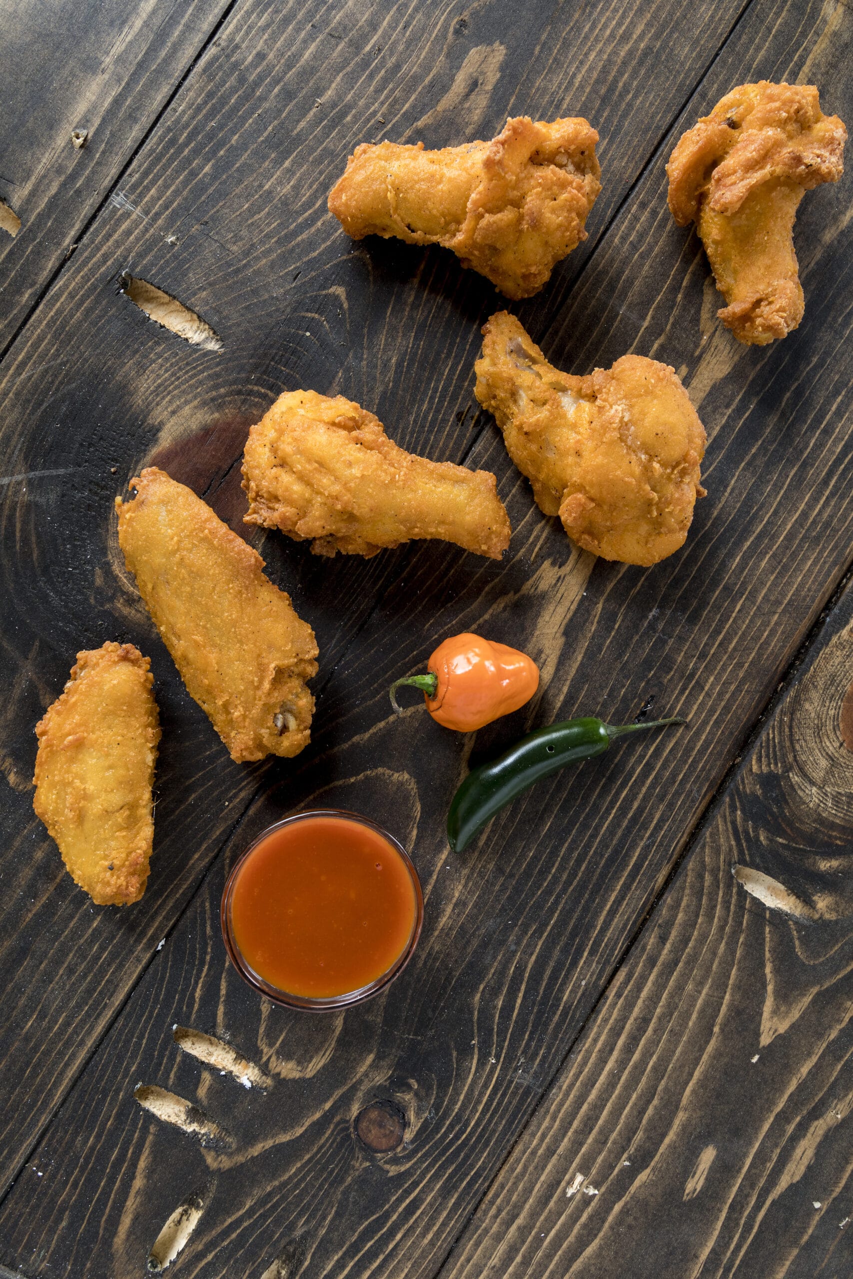 6 chicken wings and drums on a wooden table with peppers and a dipping sauce