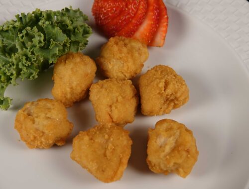 White plate with chicken nuggets and a sliced strawberry