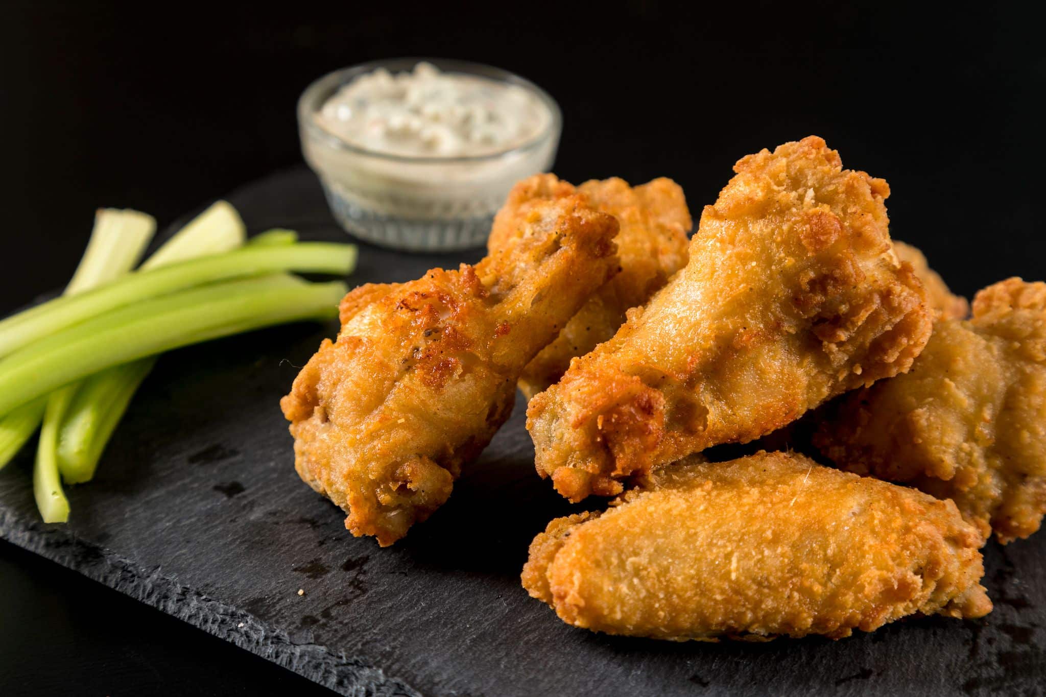 Photo of chicken wings and drums on a black slate tray, served with celery and sauce